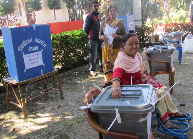 A female wheelchair user places her vote into a ballot box in Nepal