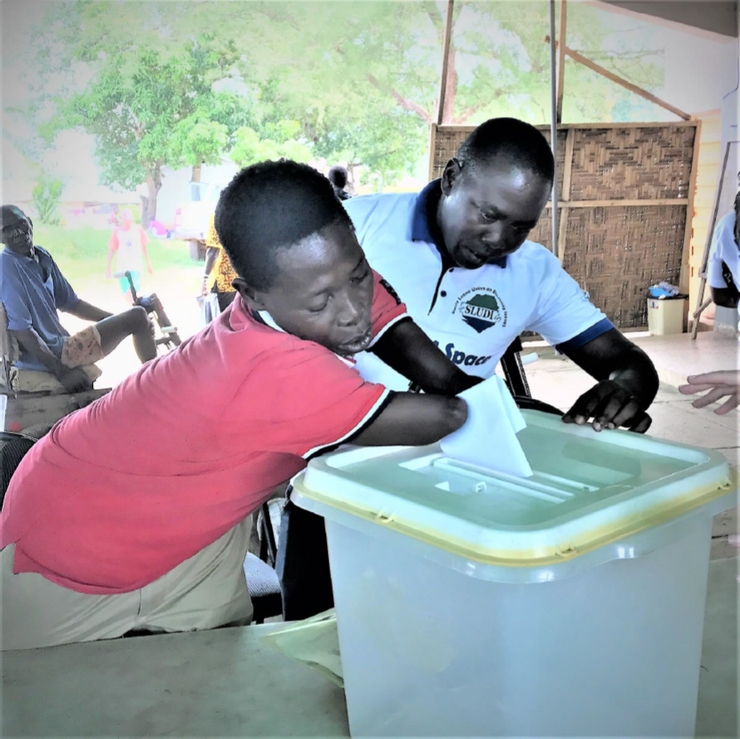 A young man without forearms places his ballot into a ballot box