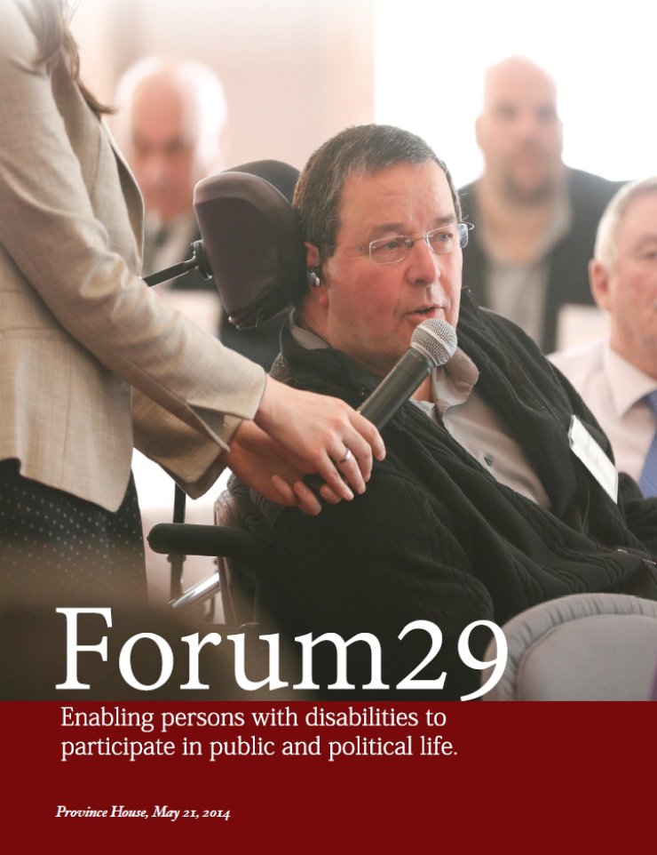 A man using a wheelchair leans to his right to speak into a microphone